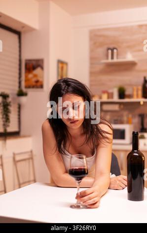 Une femme boit seule à cause de la solitude et de la dépression, montrant un comportement malsain, de l'anxiété et une épuisement émotionnel, avec le contexte soutenu de dépendance et de santé émotionnelle préservé. Banque D'Images