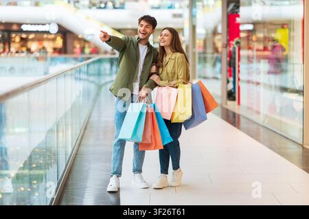 Jeunes couples heureux faisant leurs courses ensemble au centre commercial, portant des sacs de shopping colorés Banque D'Images