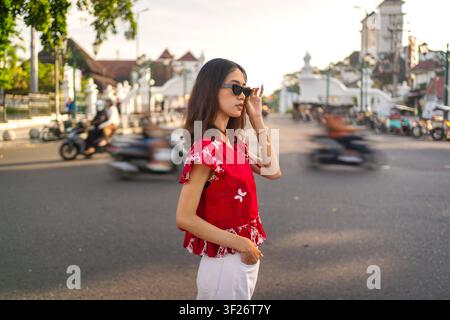 Jeune Indonésienne portant une mode batik moderne et des lunettes de soleil dans une scène de rue urbaine vibrante à Yogyakarta. Banque D'Images