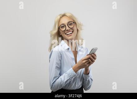 Jeune femme souriante tenant un smartphone et envoyant des messages, concept commercial Banque D'Images