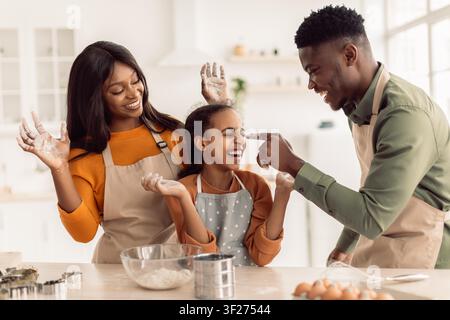 Famille noire heureuse cuisinant ensemble dans la cuisine, souriant et s'amusant Banque D'Images