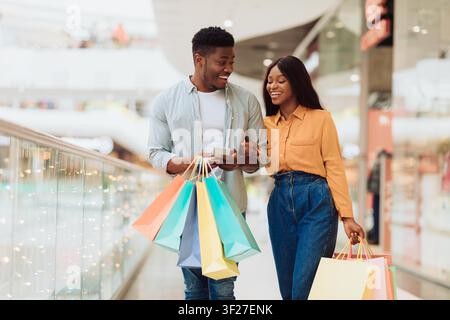 Couple noir heureux faisant des achats ensemble dans un centre commercial avec des sacs de shopping colorés Banque D'Images