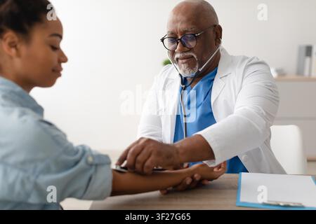 Docteur noir vérifiant la tension artérielle d'une jeune femme dans une clinique, concept de soins de santé Banque D'Images
