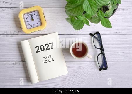 Message « 2027 Nouveaux Objectifs » sur un bloc-notes ouvert, à côté d'une tasse de café, de lunettes et d'une plante. Banque D'Images