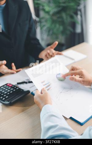 Des personnes d'affaires examinant un rapport financier avec des graphiques et une calculatrice lors d'une réunion de bureau, représentant une consultation comptable, une analyse des ventes et Banque D'Images
