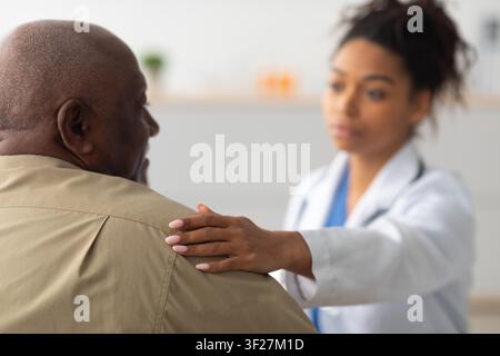 Professionnelle de santé féminine soutenant un patient masculin noir dans une clinique, interaction compatissante Banque D'Images
