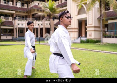 Deux athlètes karatéistes indonésiens asiatiques pratiquant le kata de karaté en plein air dans un cadre tropical, démontrant la discipline, la coordination et la concentration des arts martiaux Banque D'Images