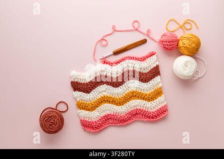 Projet de crochet coloré avec des boules de laine et un crochet sur un fond rose pastel. Projet de crochet DIY avec de la laine colorée et un crochet, flat lay. Banque D'Images