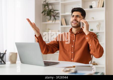 Jeune homme sud-asiatique frustré téléphonant dans un bureau à domicile, concept commercial Banque D'Images
