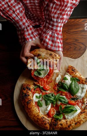 Une jeune femme prend une part de pizza fraîchement cuite. Banque D'Images