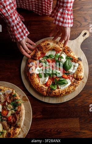 Une jeune femme prend une part de pizza fraîchement cuite. Banque D'Images