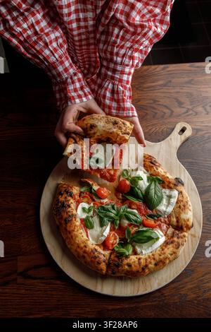 Une jeune femme prend une part de pizza fraîchement cuite. Banque D'Images