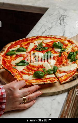 Une jeune femme prend une part de pizza fraîchement cuite. Banque D'Images