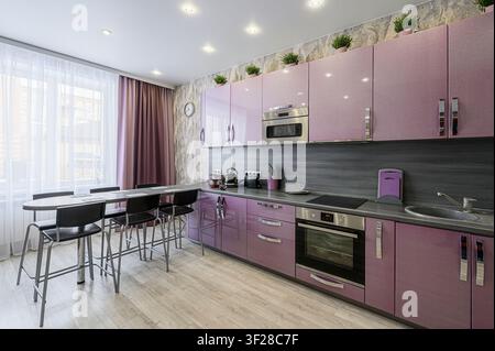 Cuisine moderne avec des armoires lilas, un plan de travail gris épuré et des sièges de style bar près d'une fenêtre lumineuse Banque D'Images