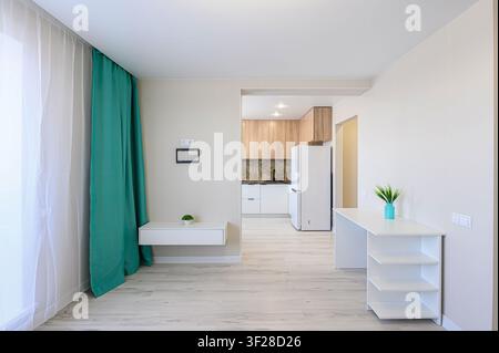 Un appartement studio lumineux et moderne avec un aperçu d'une cuisine. Les caractéristiques incluent des murs de couleur claire, des sols semblables au bois et des meubles simples Banque D'Images