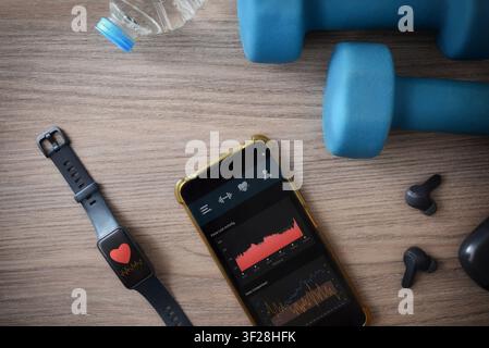 Surveillance de l'entraînement sportif sur un smartphone avec une application de suivi d'activité et une montre intelligente avec moniteur de fréquence cardiaque sur une table en bois avec des haltères Banque D'Images