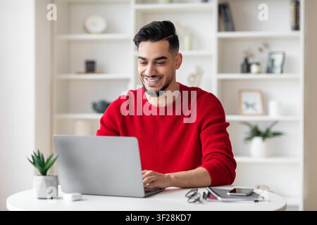 Jeune homme arabe souriant travaillant sur un ordinateur portable à la maison, concept d'affaires Banque D'Images