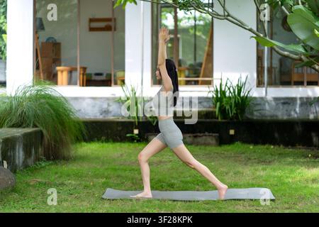 Une Indonésienne réalise une pose de yoga d'équilibre sur un tapis dans un jardin luxuriant en extérieur, mettant en valeur le calme, l'exercice et le bien-être naturel. Banque D'Images