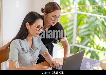 Deux femmes d'affaires examinant des informations et collaborant sur un travail d'ordinateur portable dans un espace de travail contemporain lumineux. Banque D'Images