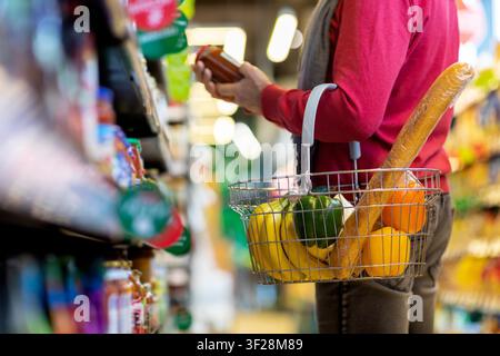 Femme non identifiable faisant ses courses dans un supermarché avec un panier rempli de fruits frais et d'une baguette Banque D'Images