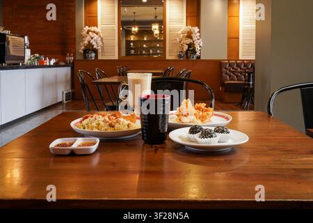 Plats asiatiques variés servis sur une table de restaurant, notamment du riz frit, des wontons croustillants, des boules de dessert au sésame, des sauces et du thé au lait dans un restaurant décontracté Banque D'Images