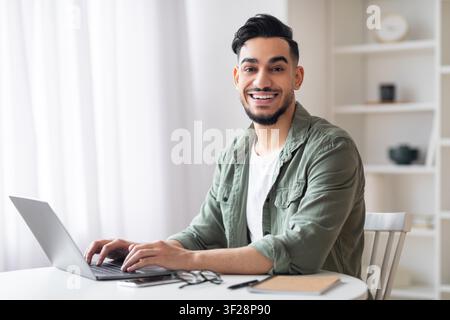 Jeune homme souriant utilisant un ordinateur portable au bureau à domicile, concept commercial Banque D'Images