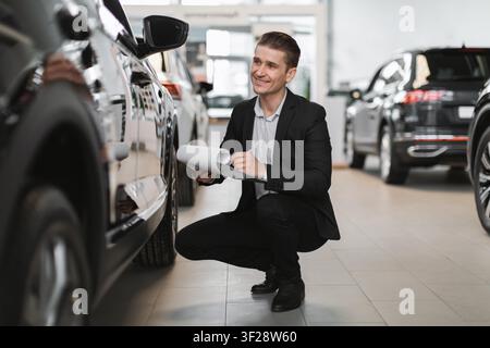 Homme souriant inspectant un véhicule chez un concessionnaire automobile, concept commercial Banque D'Images