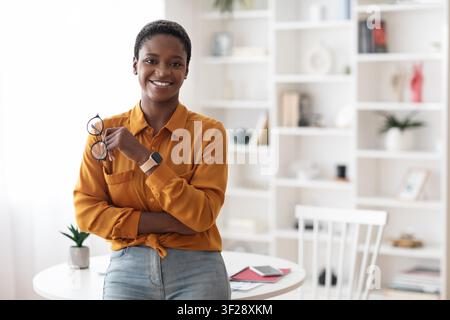 Femme noire souriante tenant des lunettes dans un bureau moderne, concept d'affaires Banque D'Images