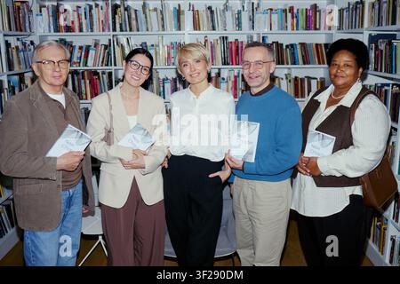 Portrait de membres adultes variés d'un club de lecture tenant des romans et se tenant dans une bibliothèque, promouvant la communauté de lecture et la culture littéraire. Idéal pour le marketing éducatif et les campagnes d'édition Banque D'Images