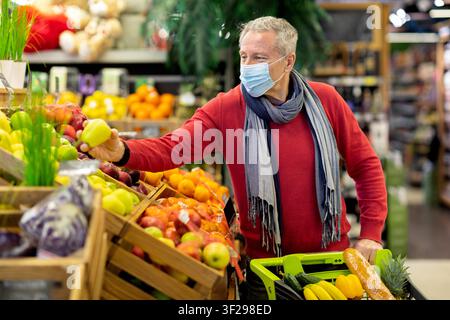 Homme caucasien âgé portant un masque et choisissant des fruits frais en faisant ses courses dans un supermarché Banque D'Images
