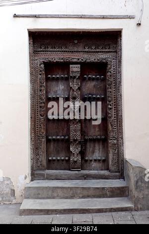 Une belle porte historique de Zanzibar en bois sombre, arborant des motifs floraux finement sculptés à la main, des clous en laiton et un poteau central orné. Le tr Banque D'Images