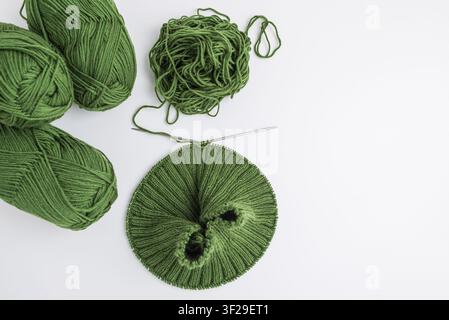 Boules de fil vert, un écheveau emmêlé et un projet de tricot inachevé sur les aiguilles montrant le processus de création de produits textiles faits à la main Banque D'Images