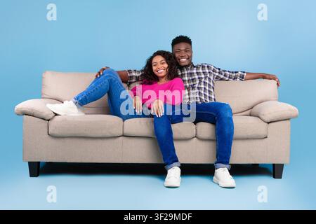 Jeun couple heureux assis sur un canapé et souriant à la maison, concept de complicité Banque D'Images