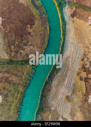 Vue aérienne d'un canal de rivière turquoise traversant un paysage rural sec Banque D'Images