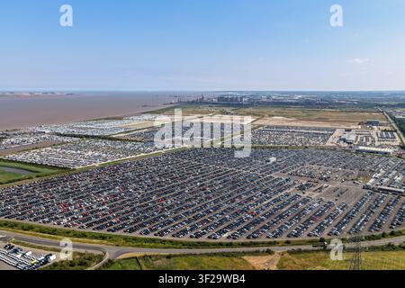 Vue aérienne de milliers de nouvelles voitures garées en rangées dans un grand centre de stockage de véhicules près de la côte sous un ciel bleu clair, Royaume-Uni. Banque D'Images