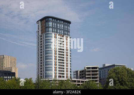 Une haute tour résidentielle moderne se détachant sur un ciel bleu clair, entourée d'autres bâtiments et d'arbres à Salford Quays, Salford, Royaume-Uni. Banque D'Images