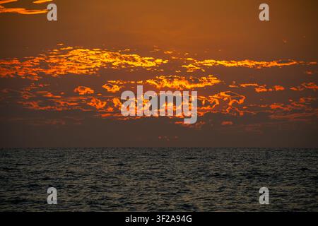 Paysage marin serein pendant le coucher du soleil, où le ciel coloré se reflète magnifiquement sur la surface calme de l'océan. Banque D'Images