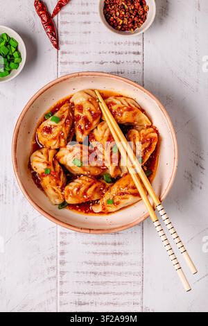 Délicieux boulettes servies dans un bol avec une sauce épicée et des oignons verts sur une table en bois Banque D'Images