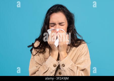 Jeune femme éternuant et utilisant un mouchoir, concept de maladie et d'allergie Banque D'Images