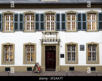 Vue de la maison Karl Marx avec sa façade blanche, sa porte en bois sombre, ses volets gris et ses fenêtres grillagées à Trèves, Rhénanie-Palatinat, Allemagne. Banque D'Images