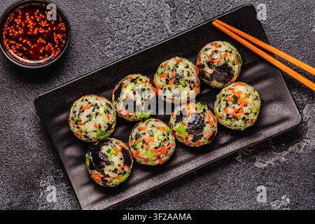 Boulettes de riz coréennes (jumeokbap) avec légumes servis avec sauce dans une assiette, vue de dessus. Banque D'Images