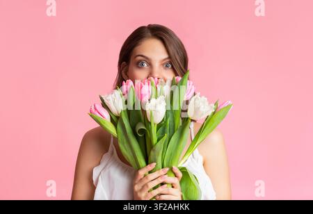 Jeune femme tenant un bouquet de tulipes roses et blanches devant un fond rose Banque D'Images