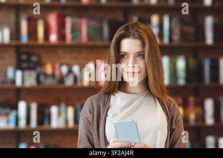 Jeune femme souriante tenant un smartphone dans un café, concept d'affaires Banque D'Images