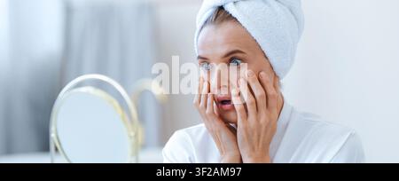 Jeune femme inquiète vérifiant son état de peau à la maison, routine de soins de la peau Banque D'Images