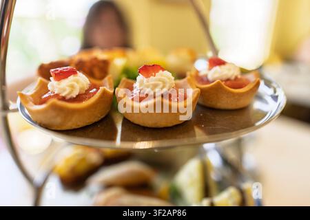 Élégant stand de thé de l'après-midi avec mini tartes aux fraises, sandwiches doigts et pâtisseries salées Banque D'Images