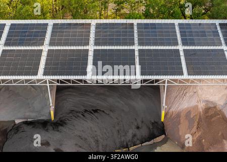 Vue aérienne de panneaux solaires installés sur une structure de toit couvrant de grands tas de matériau industriel sombre en Pologne. Banque D'Images
