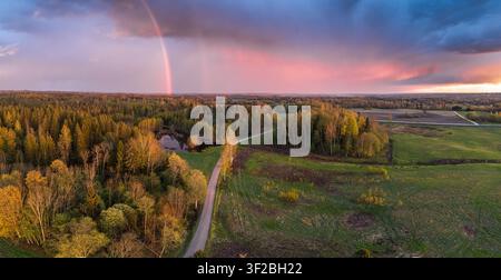 Vue aérienne d'un arc-en-ciel sur une forêt luxuriante, un petit étang et des champs ruraux en Lettonie. Banque D'Images