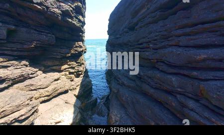 Regardant dans une fissure rocheuse étroite où l'eau claire de l'océan s'écoule entre les parois sombres et stratifiées des falaises à Hook Head Banque D'Images