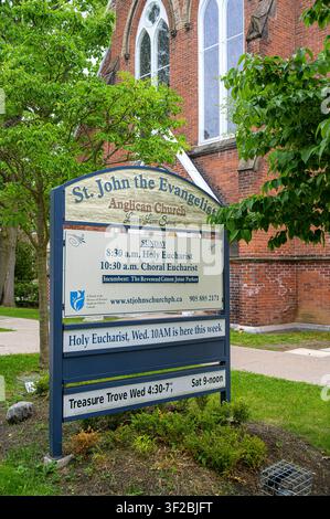 Panneau de l'église anglicane Saint-Jean l'Évangéliste devant une église historique en briques. Banque D'Images