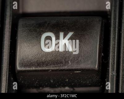 Macro prise de vue rapprochée d'un bouton en plastique texturé noir avec le mot OK illuminé en texte blanc sur le tableau de bord de l'équipement Banque D'Images